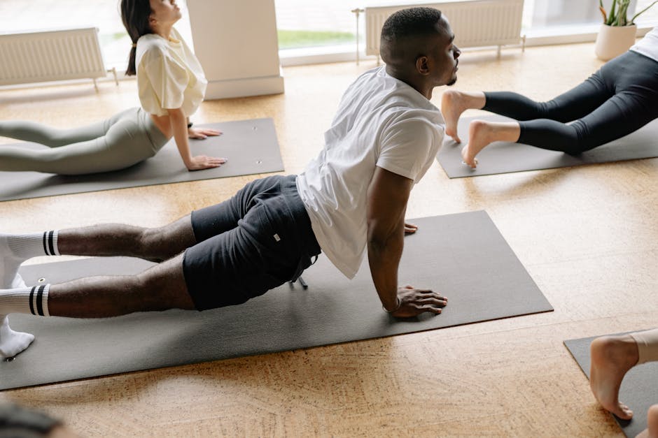 Adults in a yoga class performing stretches on mats in a well-lit studio